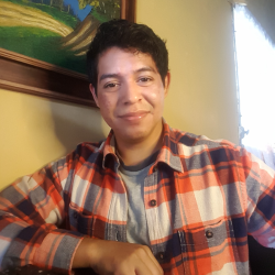 Photo of Rodrigo, he is smiling and wearing an orange, white and blue squared shirt